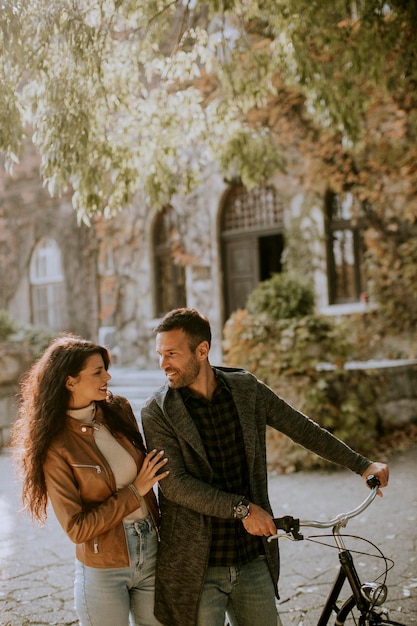 Pareja joven caminando con bicicleta en el parque de otoño