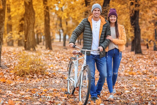 Pareja joven caminando con bicicleta a través del bosque de otoño