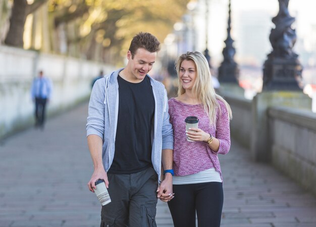 Pareja joven caminando en Londres sosteniendo una taza de té