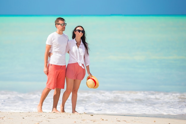 Pareja joven caminando en una playa tropical con arena blanca y agua turquesa del océano en la isla de Antigua en el Caribe