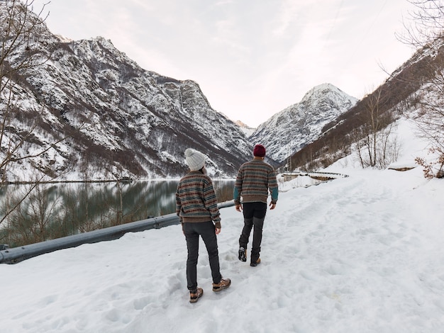 Pareja joven caminando vestida igual en ropa de invierno caminando en la nieve junto a un lago.