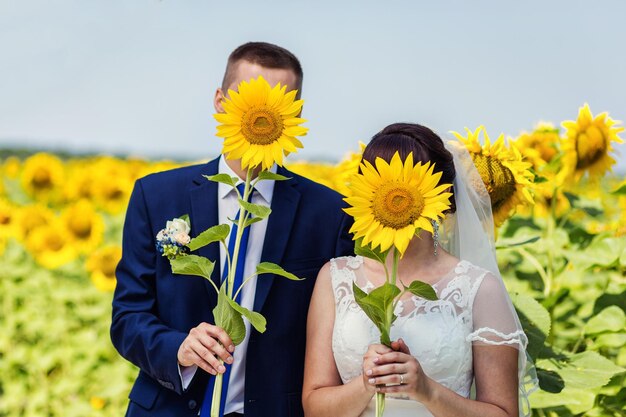 Pareja joven en un campo con girasolesRecién casados con girasoles sol campo campo de verano flores brillantes girasoles