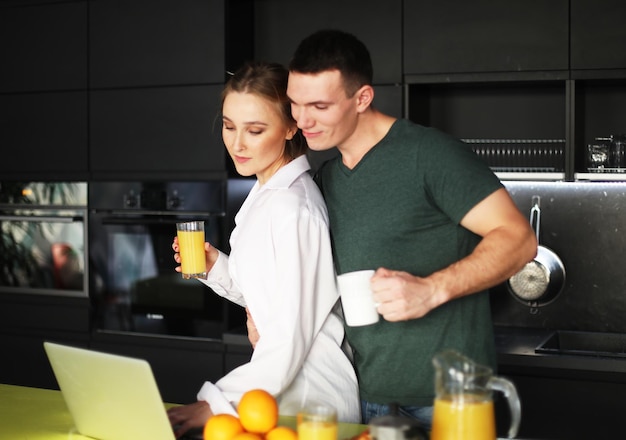 Pareja joven en casa tomando café en la cocina y trabajando en una computadora portátil