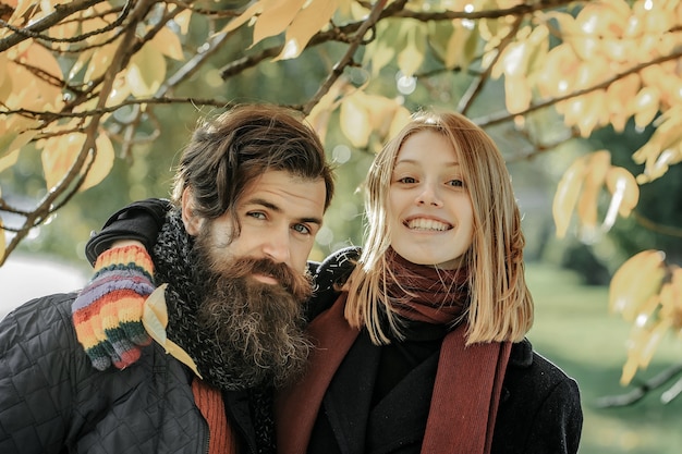 Pareja joven de chica guapa y hipster hombre barbudo al aire libre en el parque otoño con hojas amarillas sobre fondo natural en guantes de colores