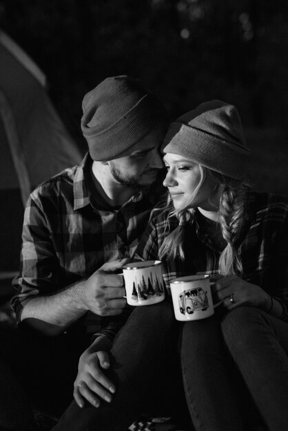 Pareja joven un chico y una chica con sombreros de punto brillantes se detuvo en un campamento cerca del fuego