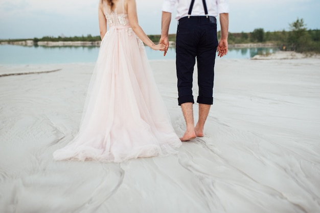 Pareja joven un chico con pantalones negros y una chica con un vestido rosa están caminando por la arena blanca del desierto