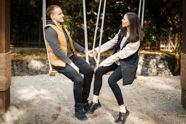 Pareja joven en una cita linda hablando mientras está sentada en un columpio en el bosque entre los árboles