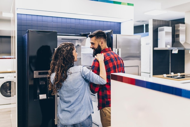 Pareja joven, clientes satisfechos eligiendo frigoríficos en la tienda de electrodomésticos.