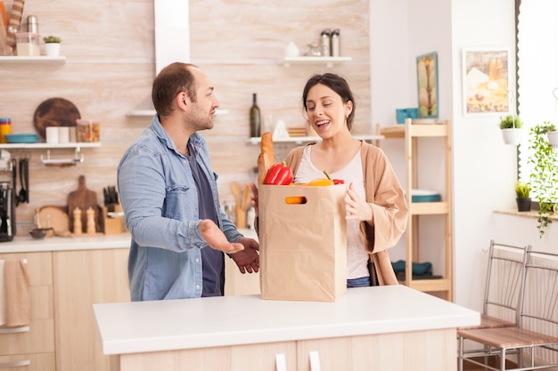 Pareja joven en la cocina con una bolsa de papel llena de comestibles del mercado. Estilo de vida de relación saludable y feliz para hombre y mujer, juntos comprando productos