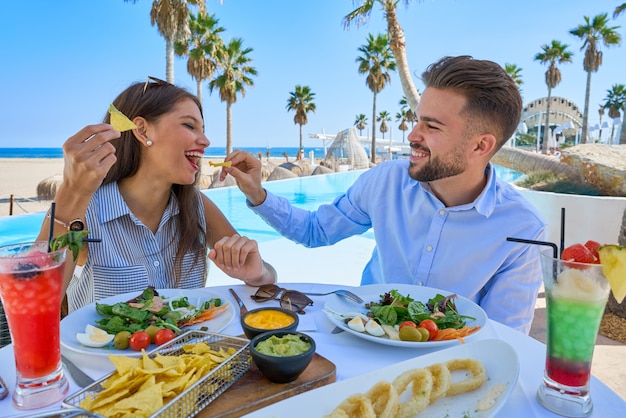 Pareja joven comiendo en un restaurante de piscina