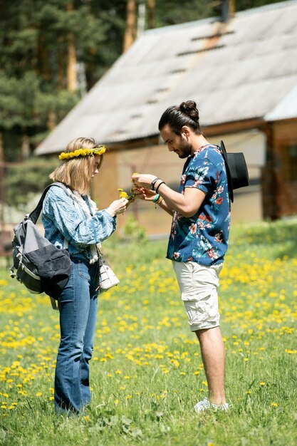 Pareja joven concentrada caminando sobre el campo de diente de león y haciendo ofrenda floral juntos