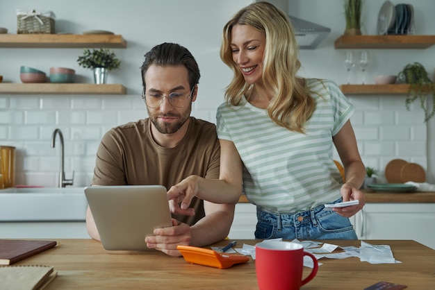 Pareja joven confiada discutiendo las finanzas del hogar en la cocina doméstica