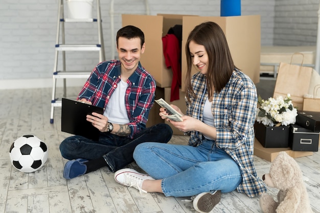 Pareja joven contando dinero mientras está sentado en el piso en un apartamento nuevo