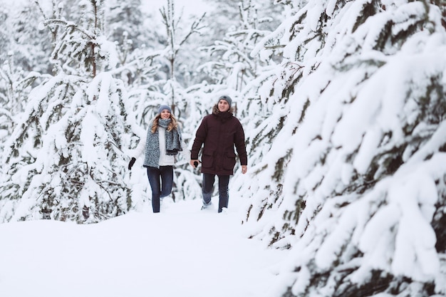 Pareja joven corriendo en un campo de invierno cubierto de nieve cerca de pino