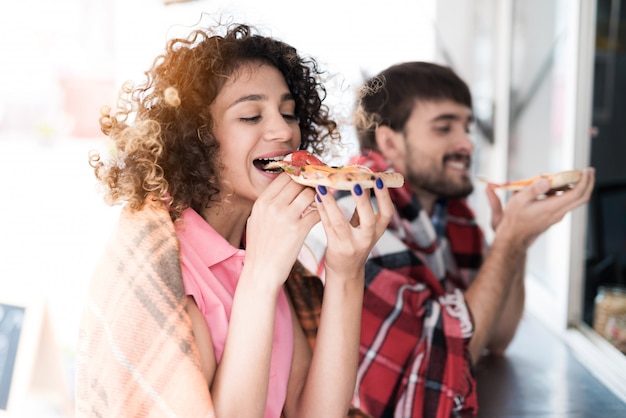 Pareja joven en cuadros cuadros comiendo pizza.