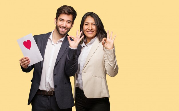 Pareja joven en el día de San Valentín alegre y confiada haciendo gesto aceptable