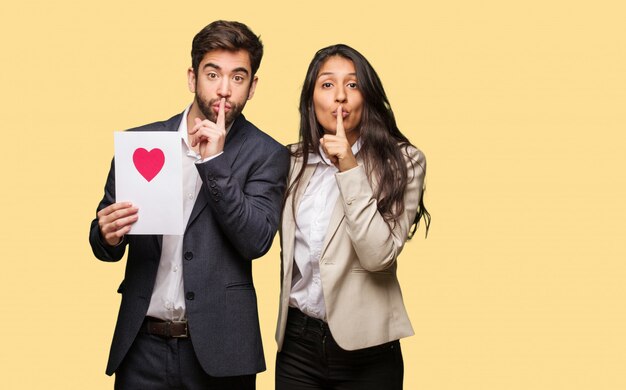 Pareja joven en el día de San Valentín guardando un secreto o pidiendo silencio