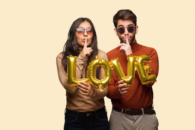 Pareja joven en el día de San Valentín guardando un secreto o pidiendo silencio