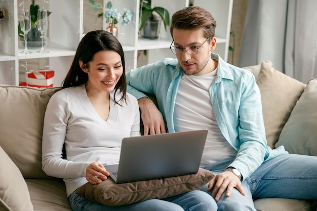 Una pareja joven disfruta de teleconferencias sociales con su familia a través de la pantalla de una computadora portátil en el distanciamiento social del condominio