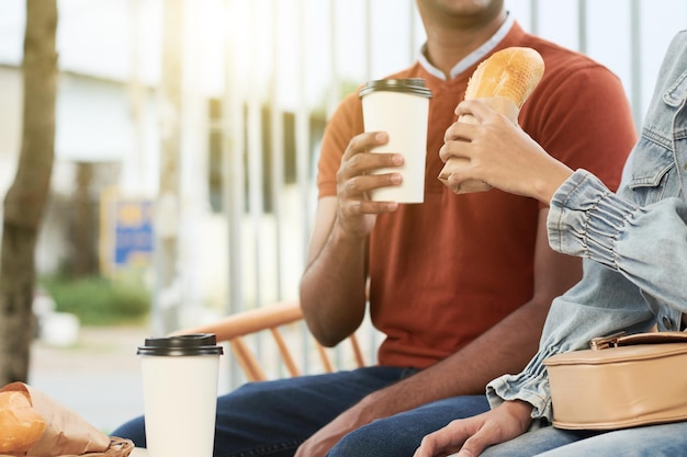 Pareja joven disfrutando de café y sándwiches cuando se sienta al aire libre