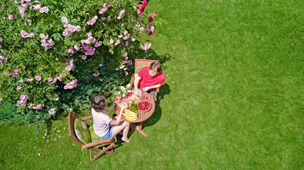 Pareja joven disfrutando de comida y bebida en el hermoso jardín de rosas en una cita romántica, vista aérea desde arriba del hombre y la mujer comiendo y bebiendo juntos al aire libre en el parque