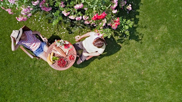 Pareja joven disfrutando de comida y bebida en el hermoso jardín de rosas en una cita romántica, vista aérea desde arriba del hombre y la mujer comiendo y bebiendo juntos al aire libre en el parque