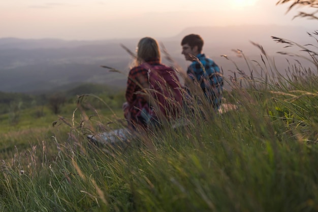 Una pareja joven disfrutando del fantástico panorama de la montaña al atardecer mientras está sentada en el banco en un