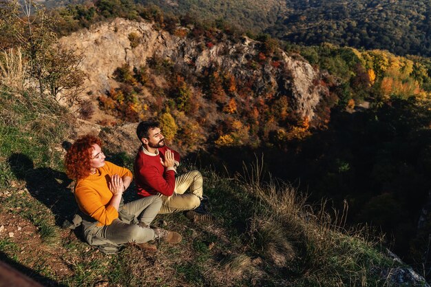 Pareja joven disfrutando de la naturaleza en un hermoso día soleado de otoño. La pareja está sentada en posición de loto y meditando en el sol.