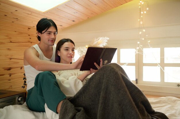 Una pareja joven divirtiéndose y disfrutando leyendo novelas populares una a la otra por la mañana en el ático