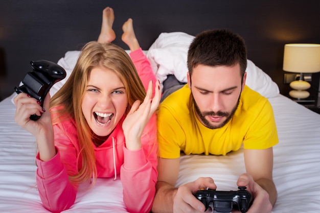 Una pareja joven divirtiéndose jugando videojuegos en la cama.