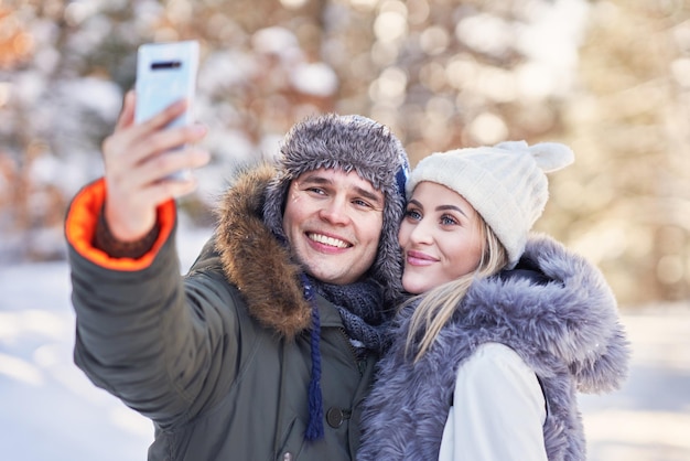 Pareja joven divirtiéndose en la nieve tomando selfie. Foto de alta calidad