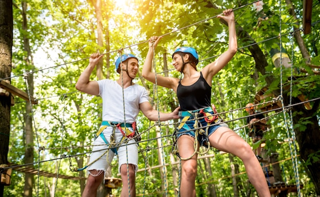 Foto pareja joven divirtiéndose en el parque de cuerdas de aventura. equipo de escalada. usar cinturón de seguridad y cascos protectores.