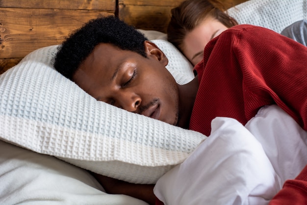 Pareja joven durmiendo en una cama.