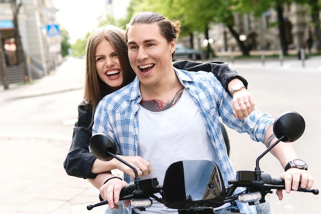 Pareja joven y elegante divirtiéndose mientras conduce scooter eléctrico en las calles de la ciudad