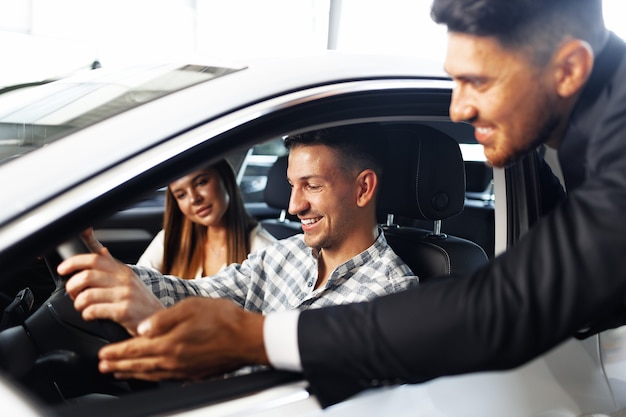 Pareja joven eligiendo un coche en el concesionario con ayuda del gerente