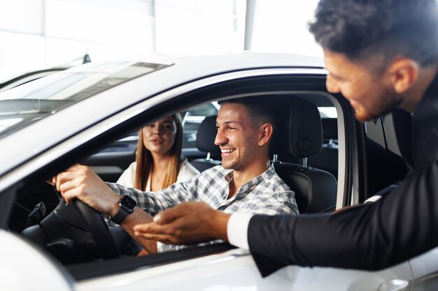 Pareja joven eligiendo un coche en el concesionario con ayuda del gerente