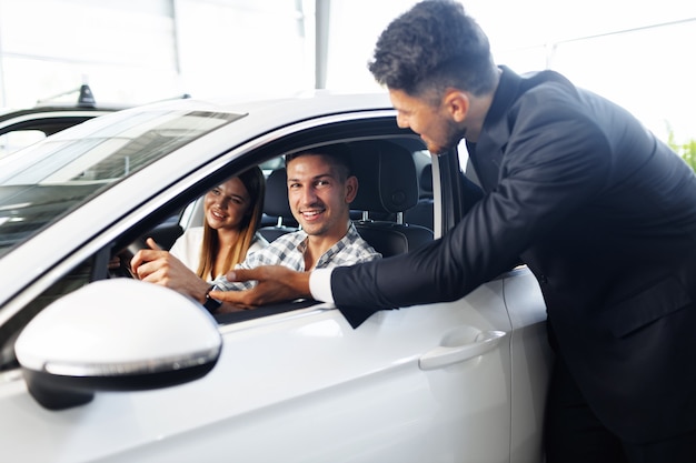 Pareja joven eligiendo un coche en el concesionario con ayuda del gerente