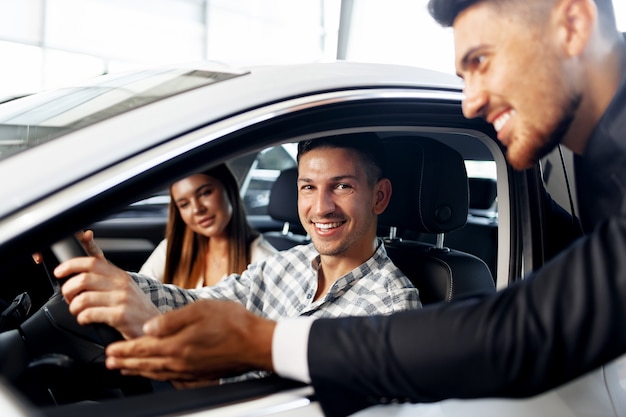 Foto pareja joven eligiendo un coche en el concesionario con el gerente ayudándoles