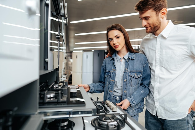 Foto pareja joven eligiendo nueva estufa de gas en la tienda de electrodomésticos