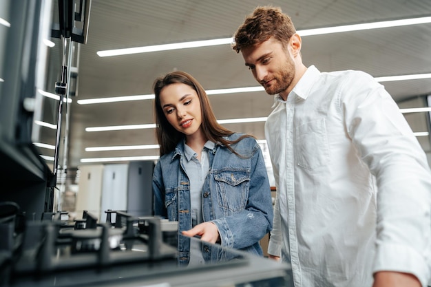 Pareja joven eligiendo nueva estufa de gas en la tienda de electrodomésticos