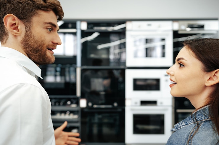 Foto pareja joven eligiendo un nuevo horno eléctrico en un hipermercado