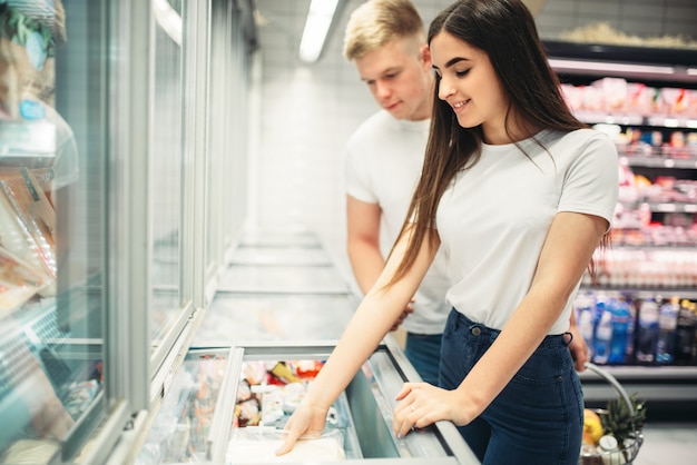 Pareja joven eligiendo productos congelados en el supermercado. Clientes en tienda de alimentos