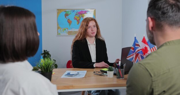 Pareja joven eligiendo un viaje con una agente sentada en la oficina de la agencia de viajes con un mapa mundial en el fondo Concepto de viaje