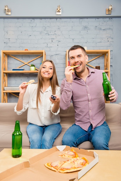 Pareja joven emocionada viendo la película con cerveza y pizza