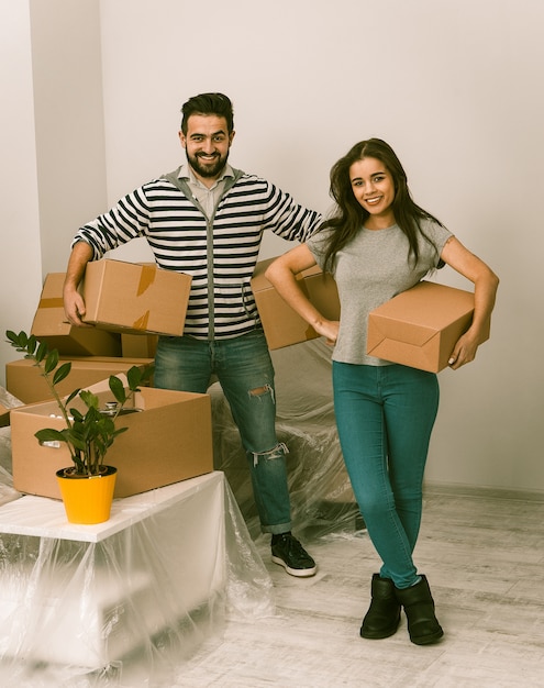 Foto pareja joven emocionado mudarse a casa de pie junto con cajas de cartón en sus manos.