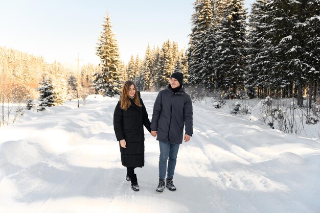 Pareja joven enamorada abrazándose en un camino nevado rodeado de paseos familiares de invierno en el bosque