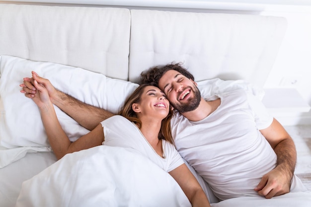 Foto una pareja joven y enamorada en la cama una pareja joven acostada en la cama y riendo mientras se hacen cosquillas una pareja joven y sensual feliz acostada juntos en la cama por la mañana
