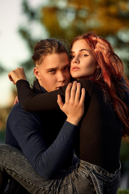 Pareja joven enamorada caminando en el parque de otoño tomados de la mano mirando la puesta de sol