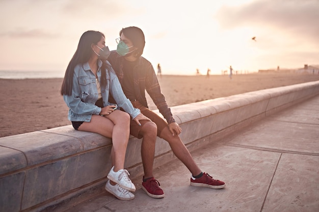 Pareja joven enamorada sentada en la playa durante una hermosa puesta de sol