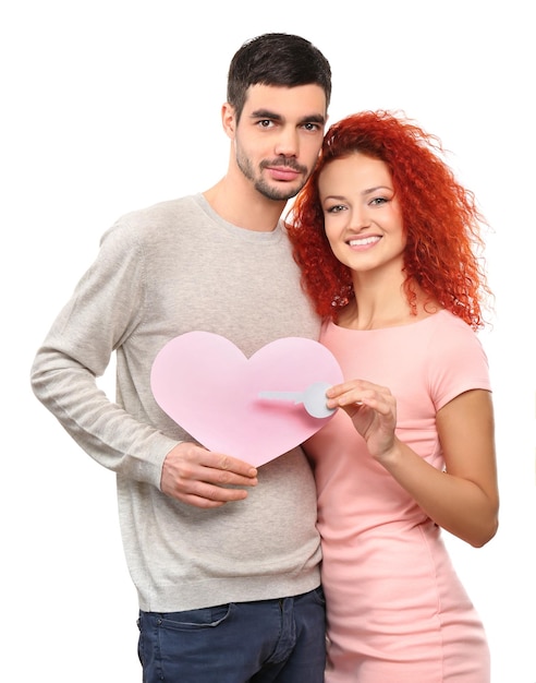 Pareja joven enamorada sosteniendo corazón rosa de papel y llave aislada en blanco